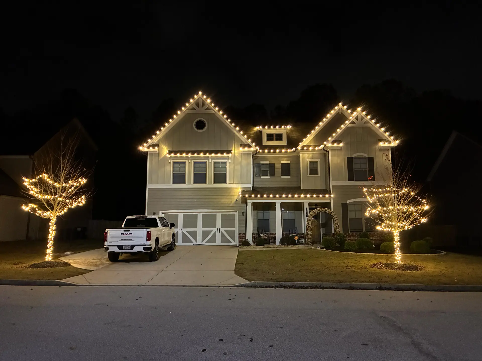Home glowing with warm white roofline Christmas lights and wrapped trees installed by Be The Light GA