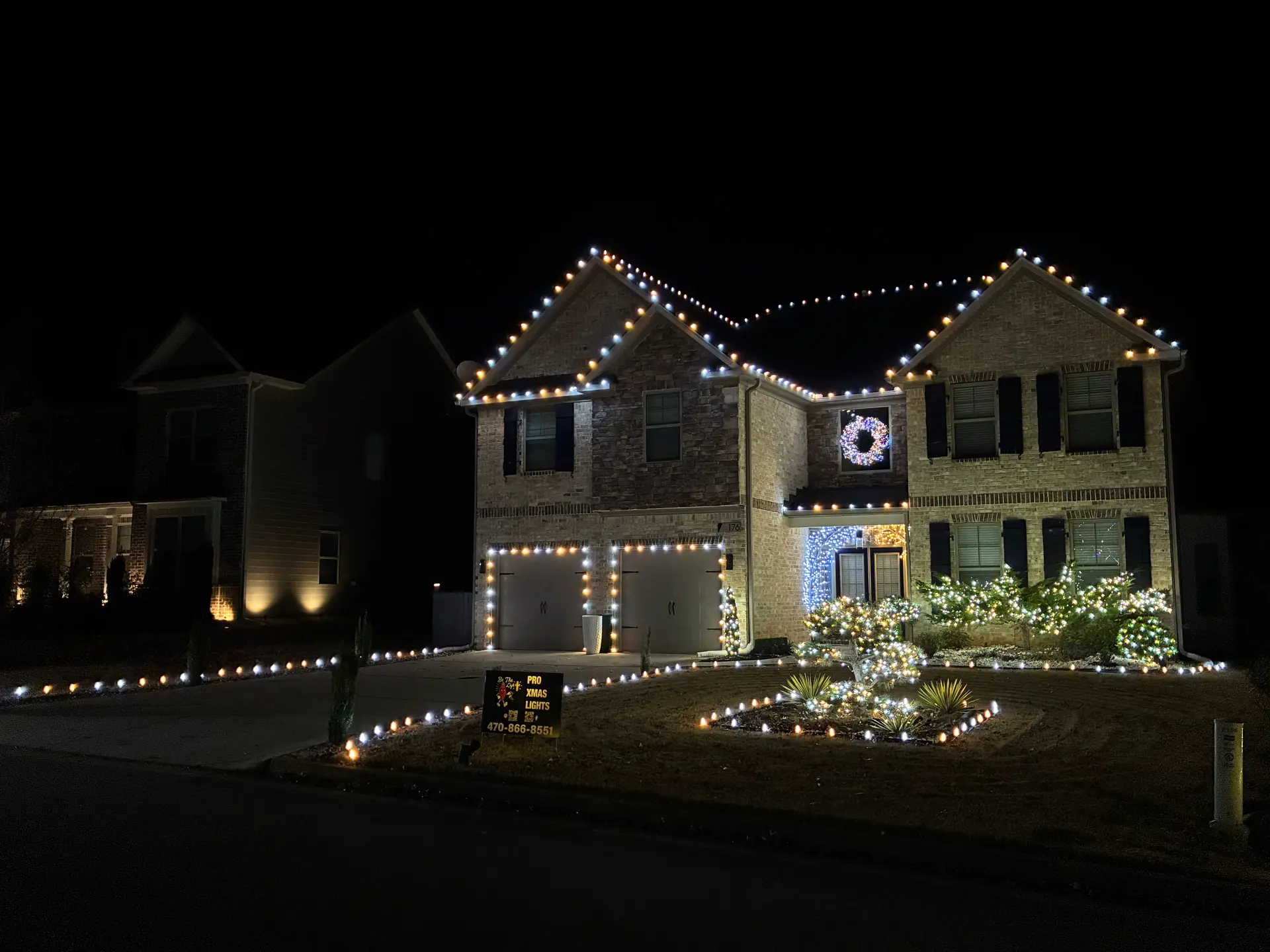 Roofline lights, a lit wreath, and glowing landscape shrubs installed by Be The Light GA