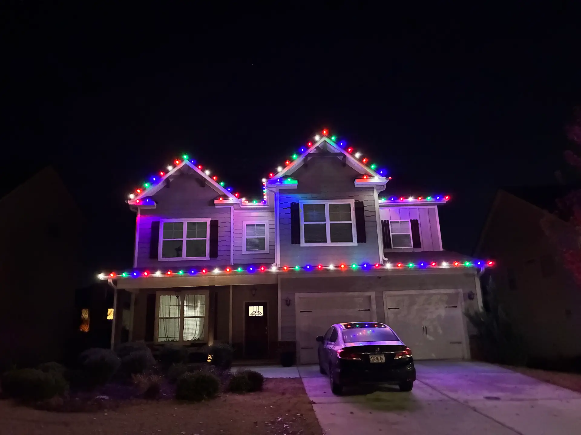 Two-story home with multicolor Christmas roofline lights by Be The Light GA